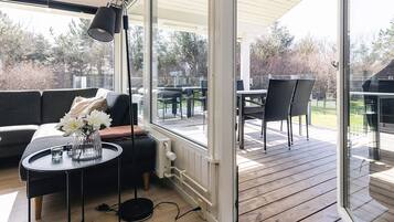 A modern outdoor seating area with a sofa, a round table, and a floor lamp, overlooking a wooden deck and garden.