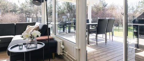 A modern outdoor seating area with a sofa, a round table, and a floor lamp, overlooking a wooden deck and garden.