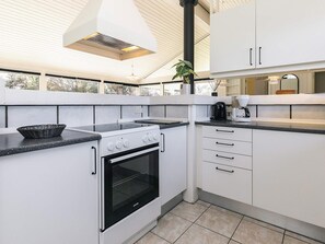 A modern kitchen with white cabinets, a black stove, and a large window. - 4 Star Holiday Home in Hjorring (Hjørring)
