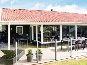 Un espace extérieur abrité, équipé de tables et de chaises, d’un barbecue et de plantes en pot.