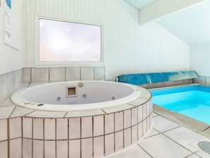 A hot tub with a tiled surround, a pool, and a ceiling with wooden panels.