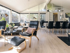 A spacious living area with a sofa, chairs, and a dining table, featuring large windows and a ceiling fan. - 4 Star Holiday Home in Hjorring (Hjørring)