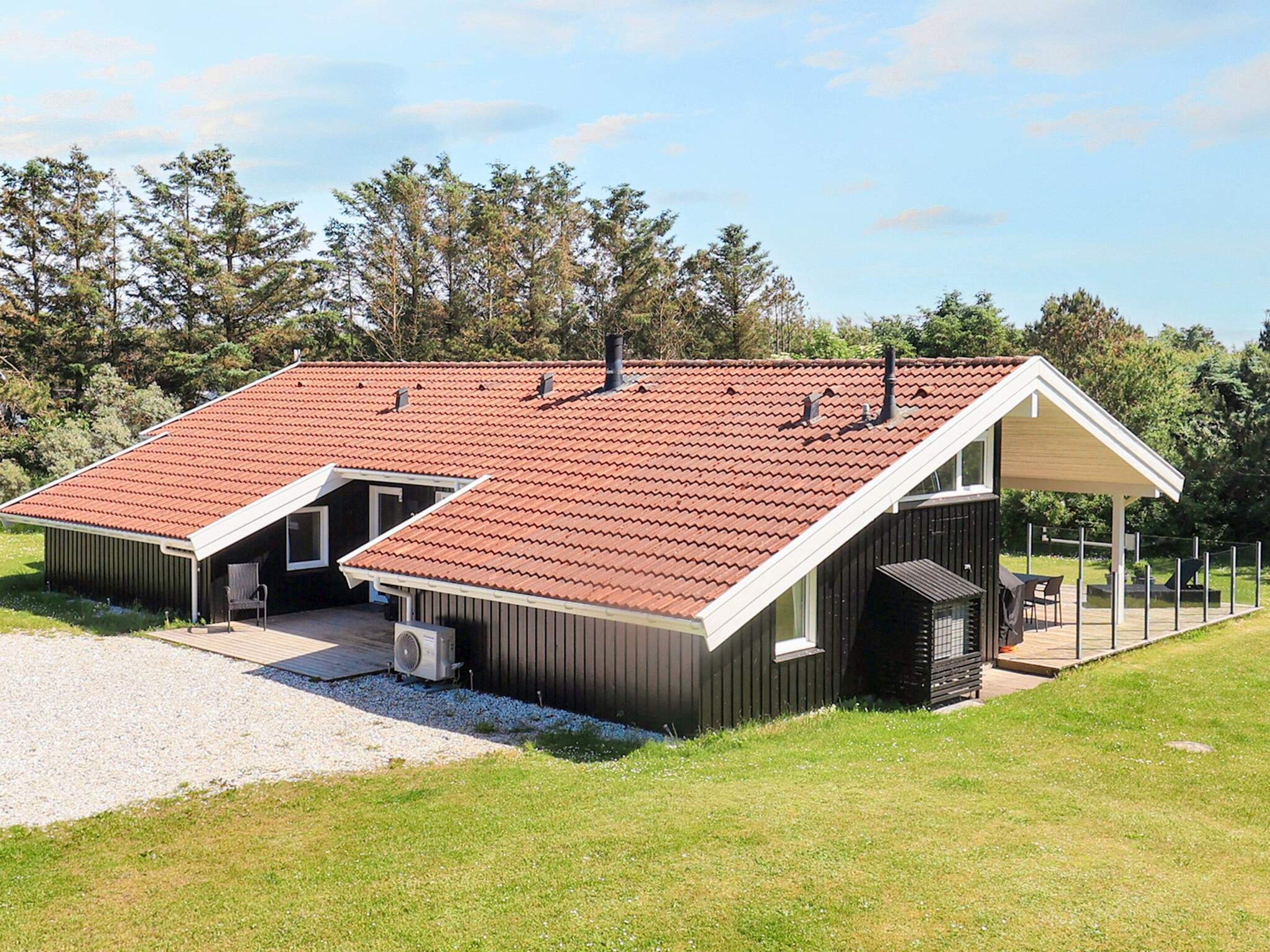 A modern building with a sloped red roof, a covered outdoor seating area, and a gravel driveway.
