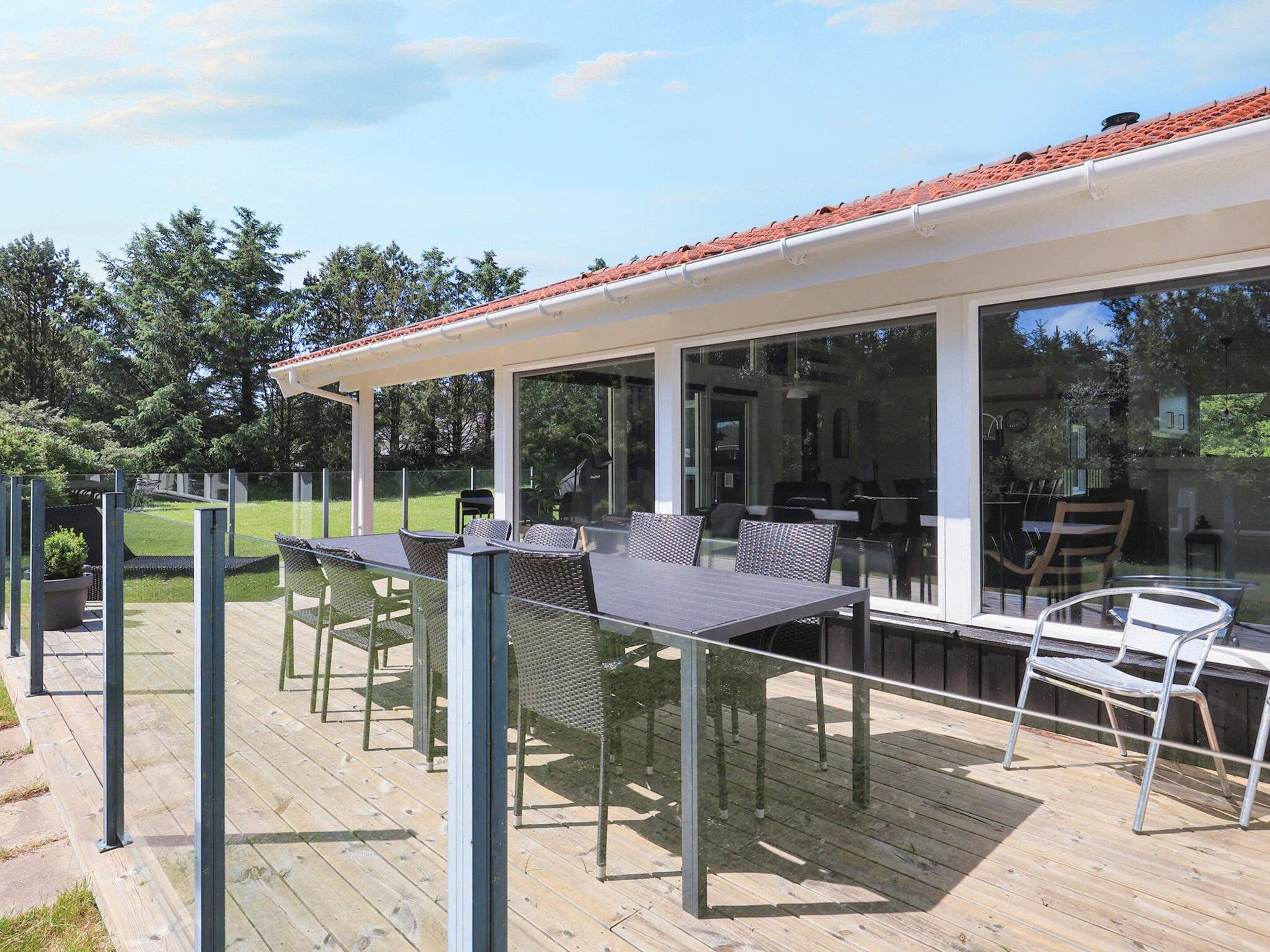 An outdoor deck with a dining area, including tables and chairs, and a glass enclosure leading to a building.
