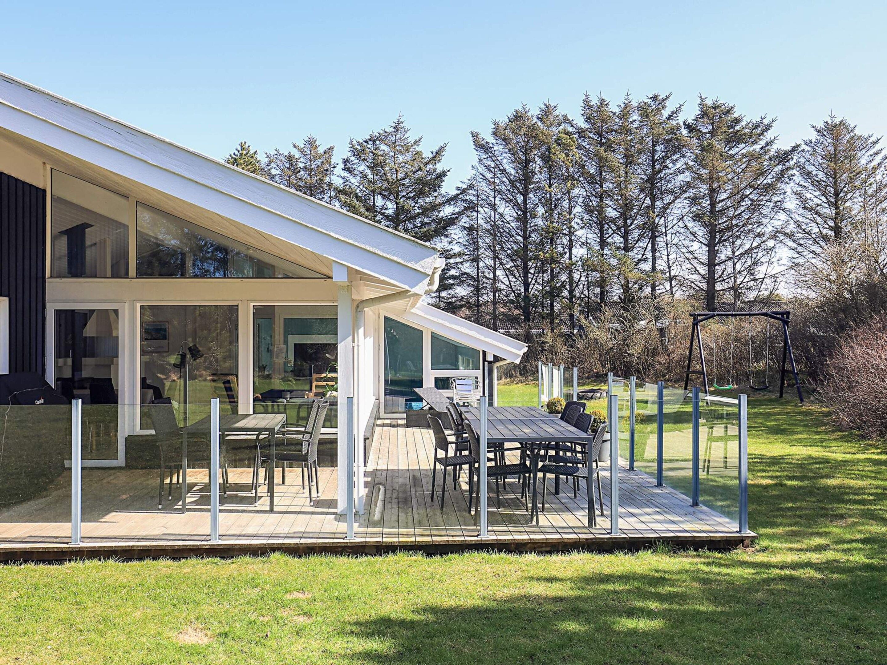 A modern house with a glass-enclosed patio, outdoor furniture, and a swing set.