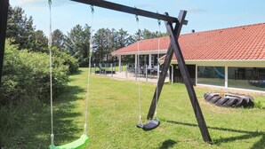 Eine Schaukel auf einer Rasenfläche, im Hintergrund ein Gebäude.