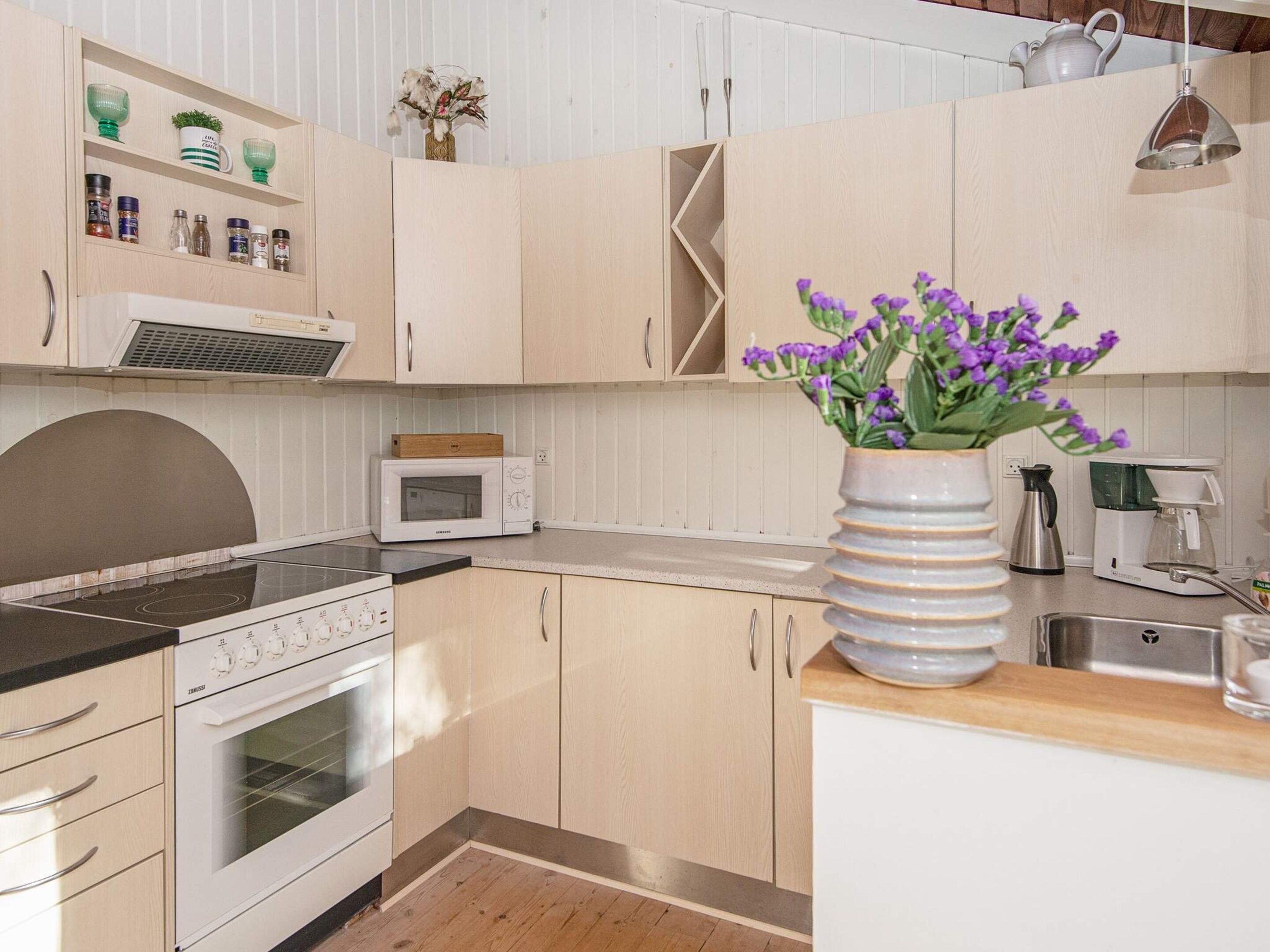 A kitchen with a microwave, stove, and a vase with purple flowers.