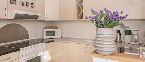 A kitchen with a microwave, stove, and a vase with purple flowers.