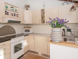 Una cocina con microondas, estufa y un jarrón con flores moradas.