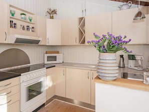 A kitchen with a microwave, stove, and a vase with purple flowers.