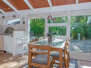 Cocina moderna con comedor, muebles de madera y ventanas grandes con vistas a un jardín.