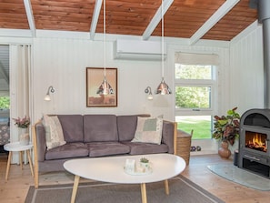 A modern living room with a sofa, a coffee table, pendant lights, a fireplace, and a large window.