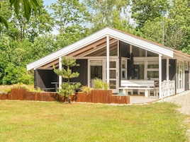 Una casa moderna con un porche cubierto, una terraza de madera y un pequeño jardín.