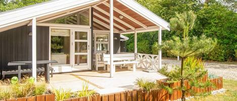 A covered outdoor seating area with a wooden deck, white railings, and a small garden.