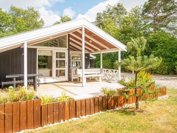 A covered outdoor seating area with a wooden deck, white railings, and a small garden.