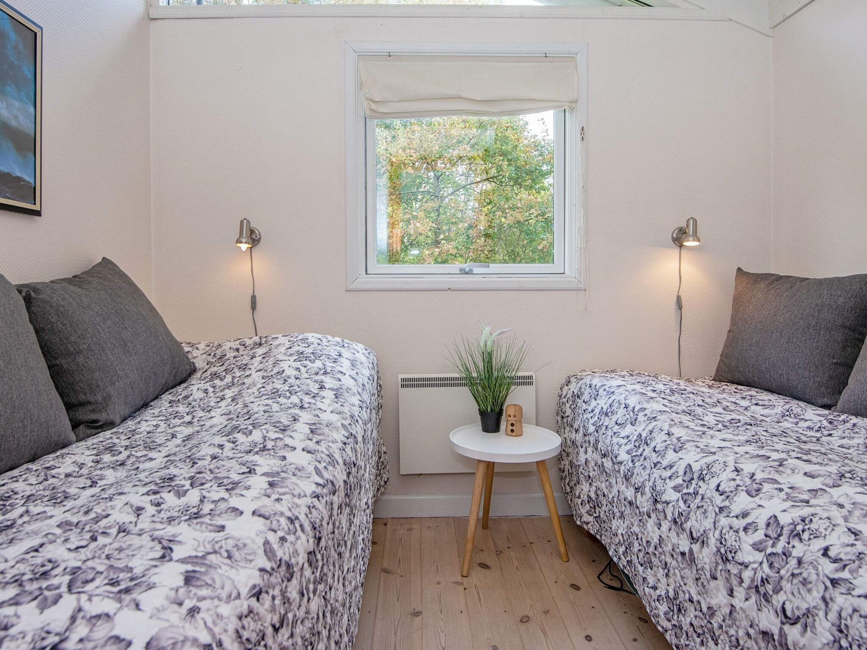A room with two beds, a small table with a plant, and a window with a view of trees.