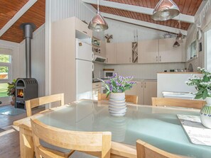 A modern kitchen with a wood stove, white cabinets, and a glass dining table.