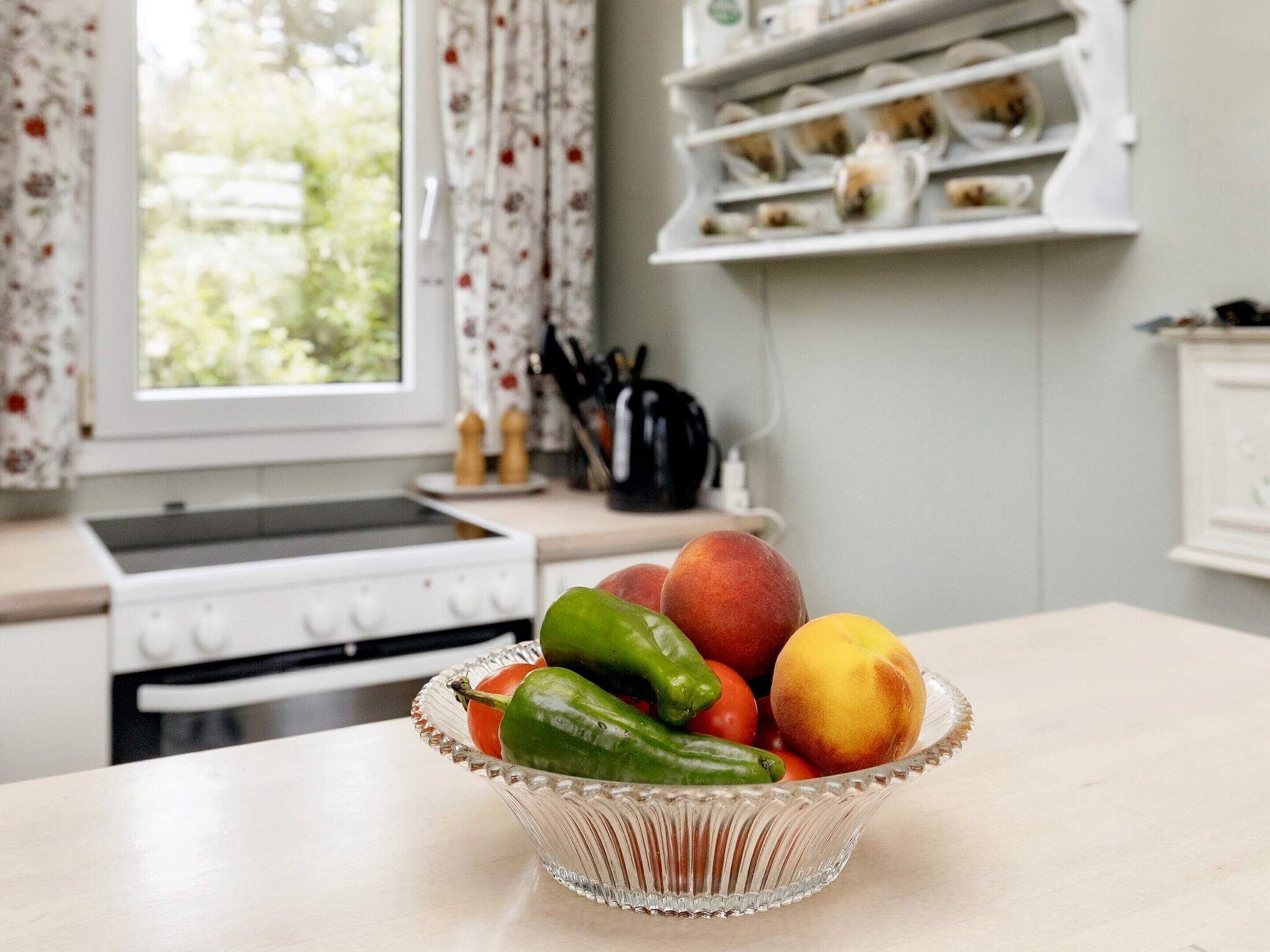 Una cucina con una ciotola di frutta sul bancone, un fornello e una finestra con tende.