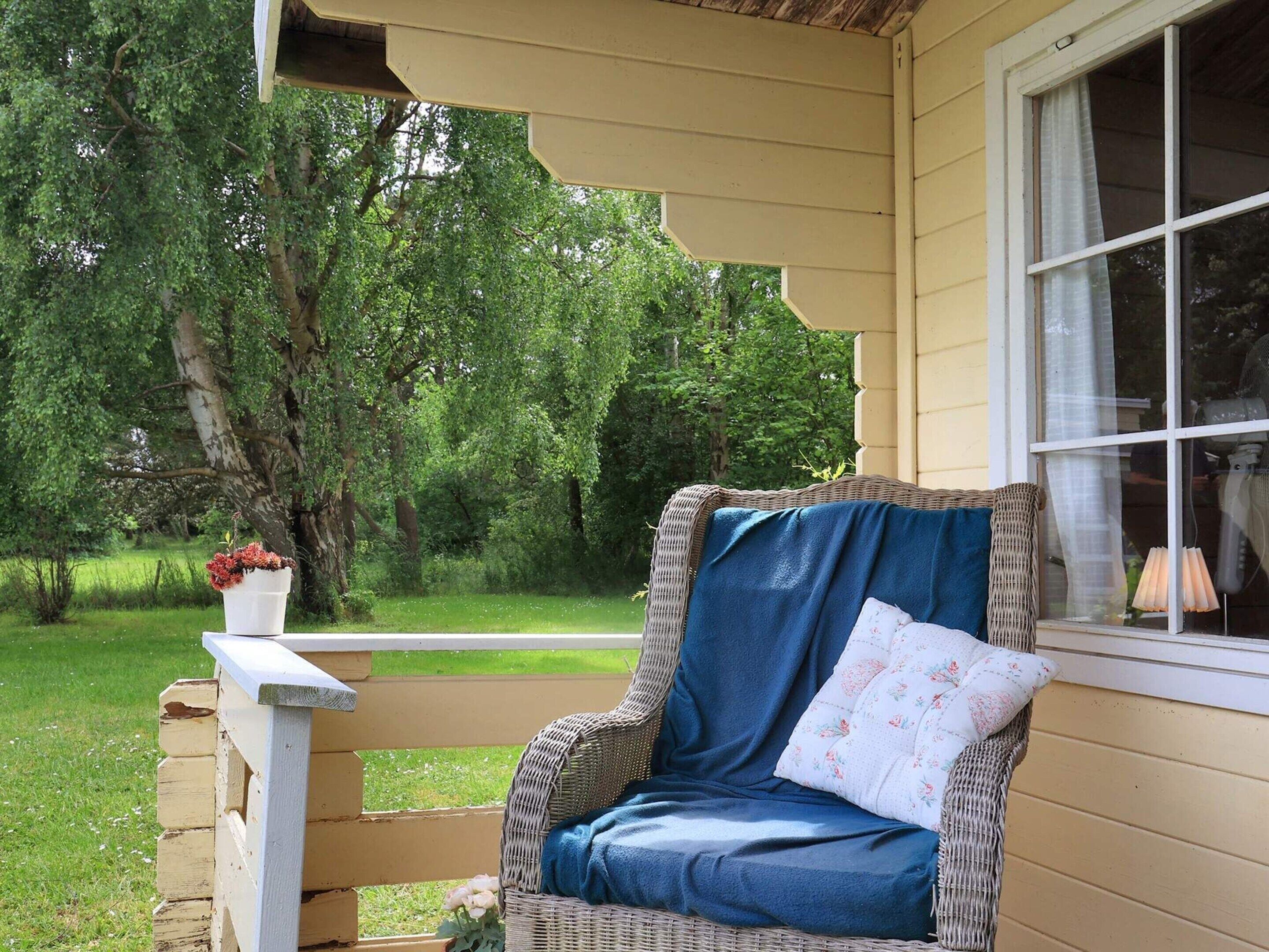 Een rieten stoel met een blauw kussen en een gebloemd kussentje, geplaatst op een veranda met een witte balustrade.
