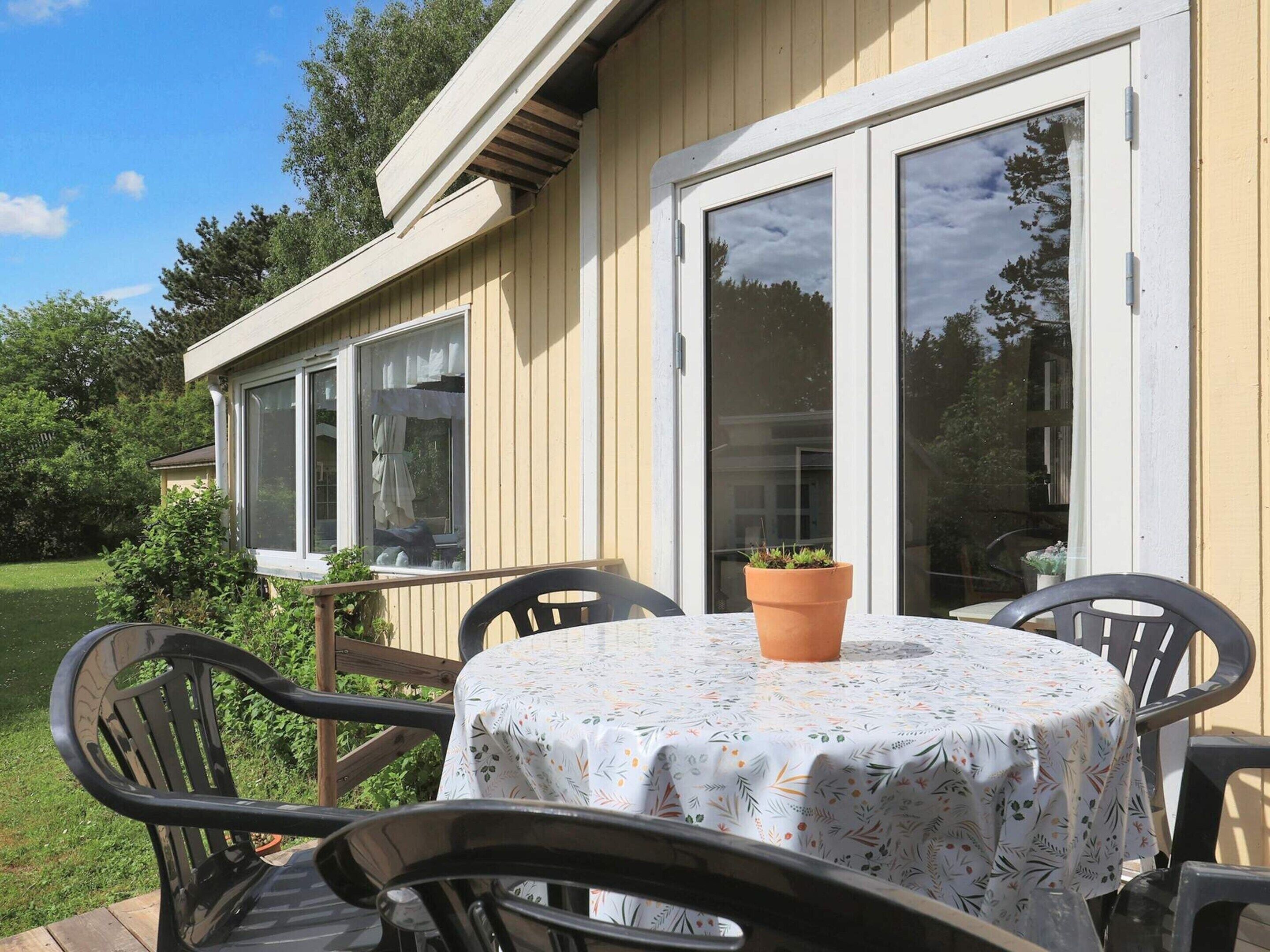Une terrasse avec une table et des chaises, un pot de fleurs et une porte-fenêtre coulissante donnant sur un jardin.