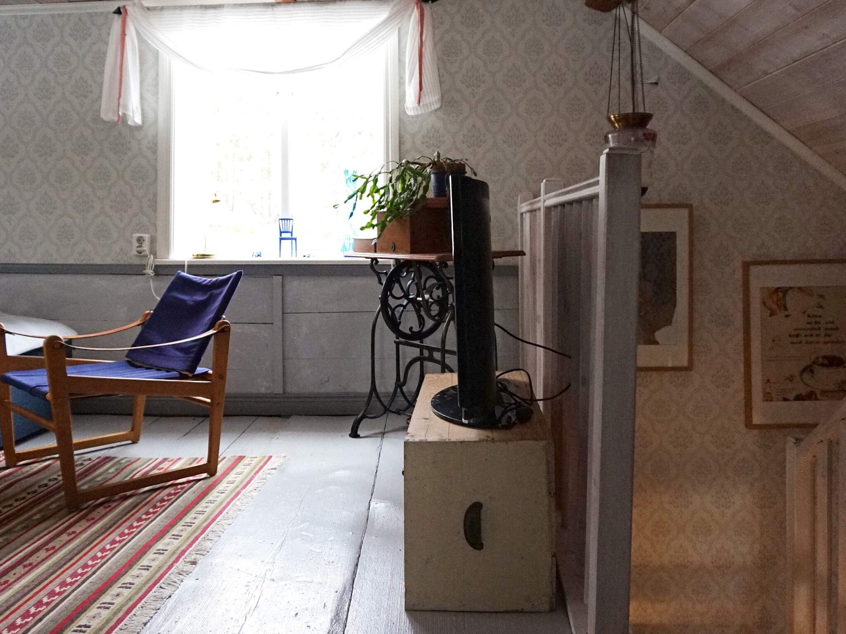 Una habitación con una silla de madera, una mesita con una planta, un televisor sobre un mueble bajo y una pared con diseño.