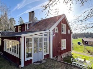 A red wooden house with a large windowed porch, a chimney, and a small garden area. - 6 Person Holiday Home in Atvidaberg-by Traum (Atvidaberg)