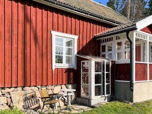 A red wooden house with a stone wall foundation, a window, and a small outdoor seating area with a table and chairs. - 6 Person Holiday Home in Atvidaberg (Atvidaberg)