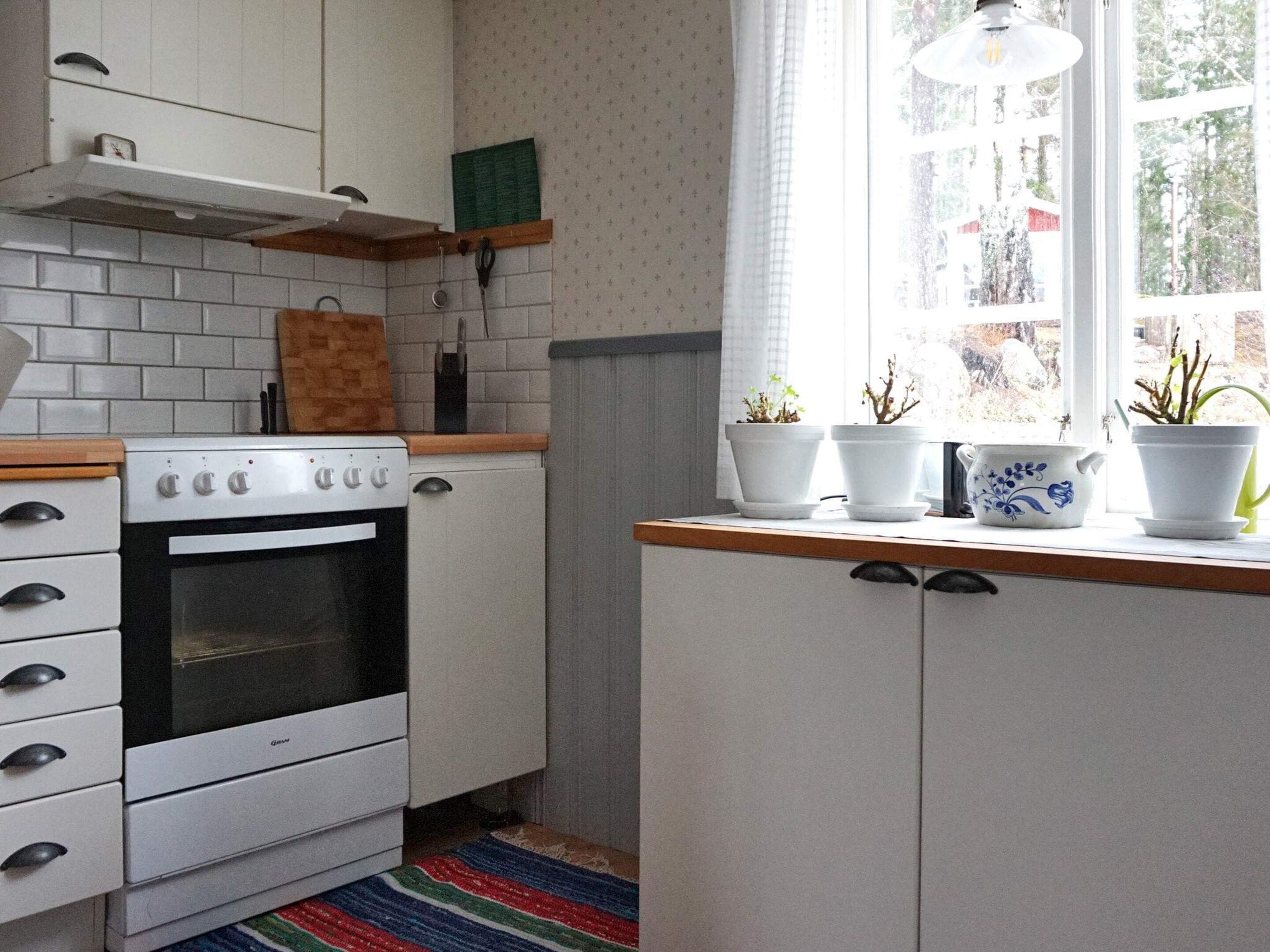 A kitchen with white cabinets, a stove, and a window with potted plants.