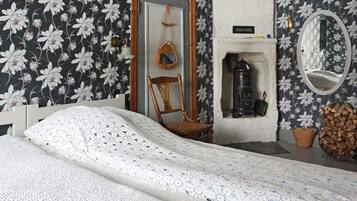 A bedroom with a bed, a chair, a mirror, a fireplace, and a wall with floral wallpaper.