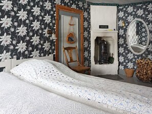 Ein Schlafzimmer mit einem Bett, einem Sessel, einem Spiegel, einem Kamin und einer Wand mit floralem Tapetenmuster.