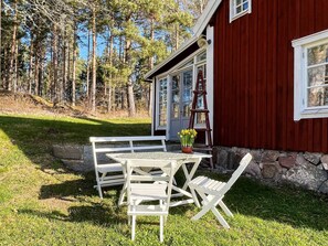 A red building with a stone foundation, a white table and chairs, and a potted plant with yellow flowers.