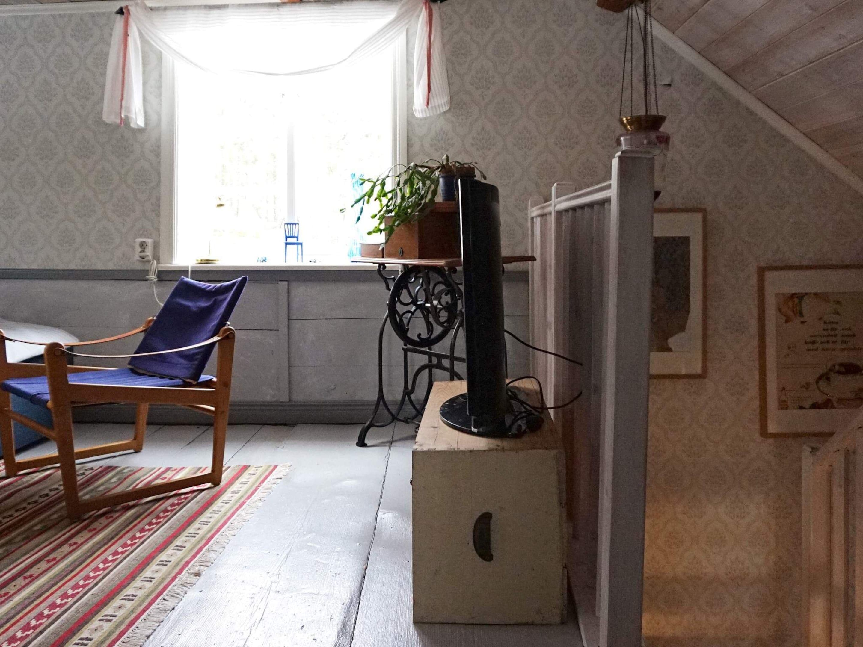 A room with a wooden chair, a small table with a plant, a television on a stand, and a patterned wall.