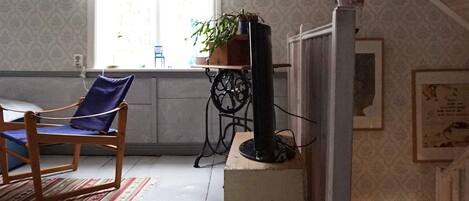 A room with a wooden chair, a small table with a plant, a television on a stand, and a patterned wall.