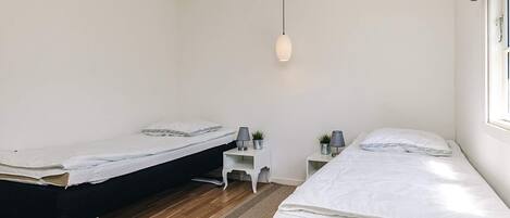 Une chambre avec deux lits, une petite table blanche, un luminaire suspendu et une fenêtre donnant sur un beau paysage.