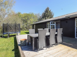 A wooden deck with outdoor furniture, a trampoline, and a building with a dark exterior and large windows.