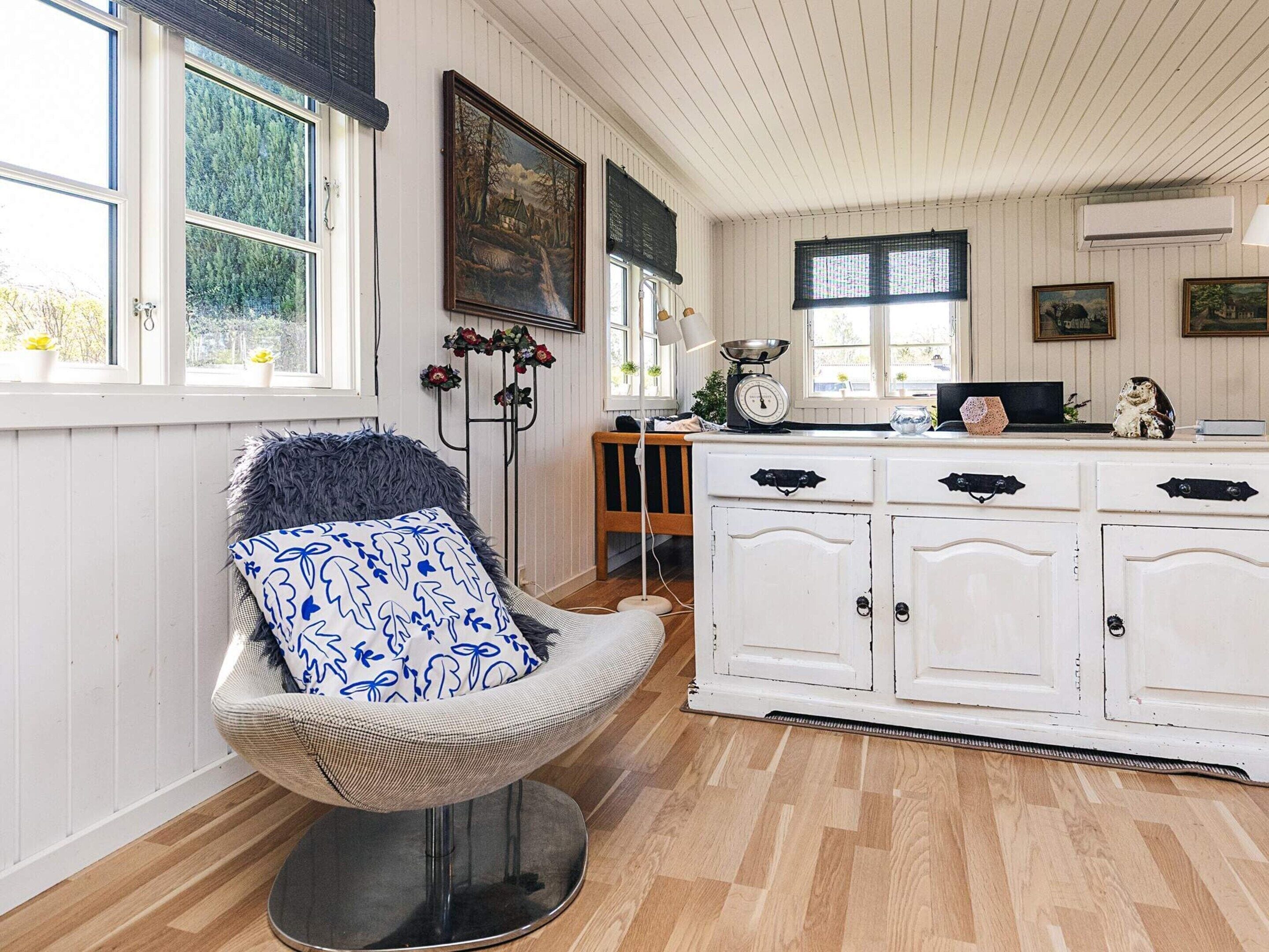 A cozy room with a chair, a white cabinet, and a window with a view of trees.