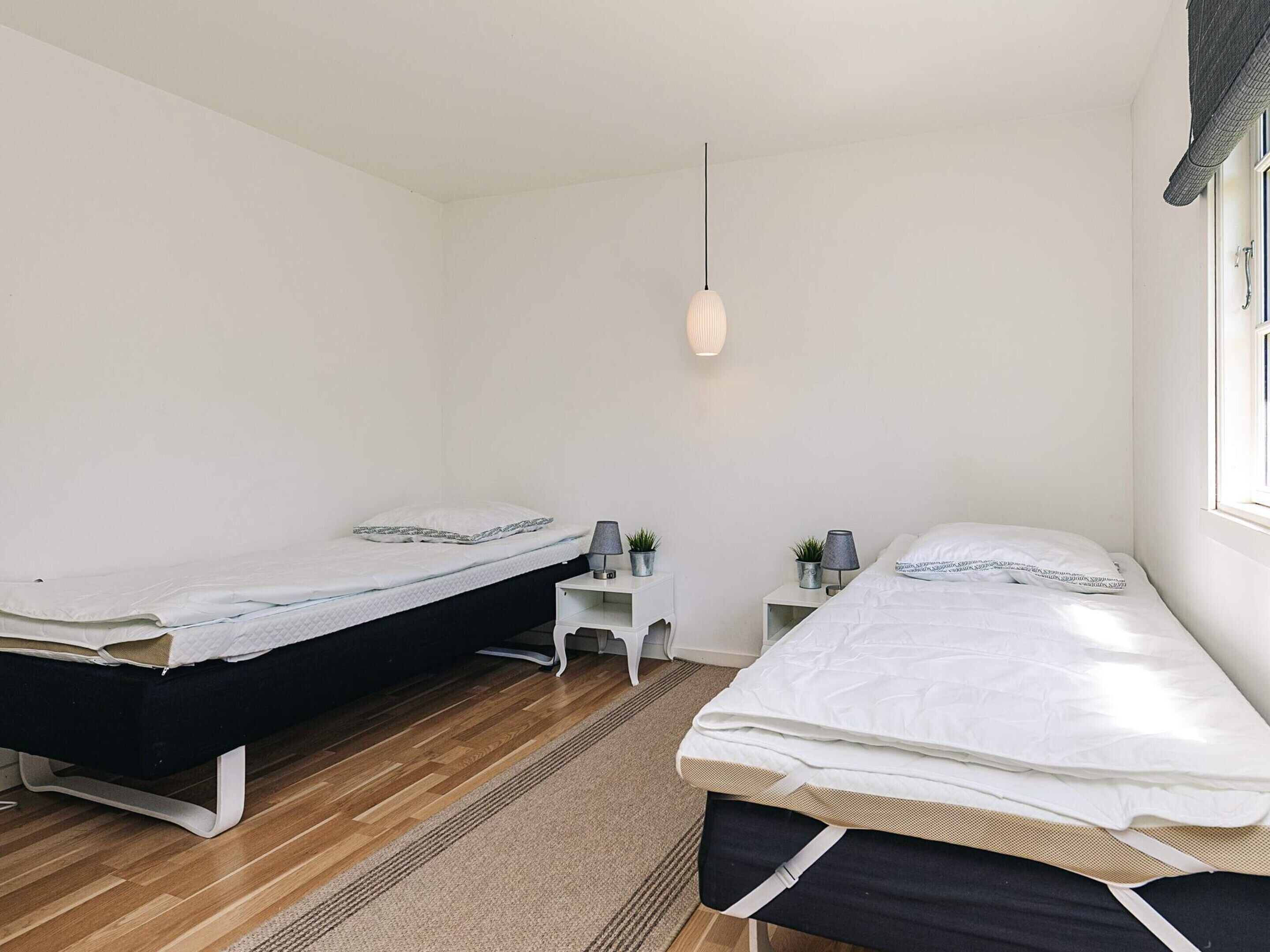 A bedroom with two beds, a small white nightstand, a hanging light, and a window with curtains.