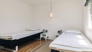 A bedroom with two beds, a small white nightstand, a hanging light, and a window with curtains.