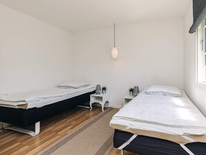 A bedroom with two beds, a small white nightstand, a hanging light, and a window with curtains. - 4 Star Holiday Home in Kirke Hyllinge (Kirke Hyllinge)