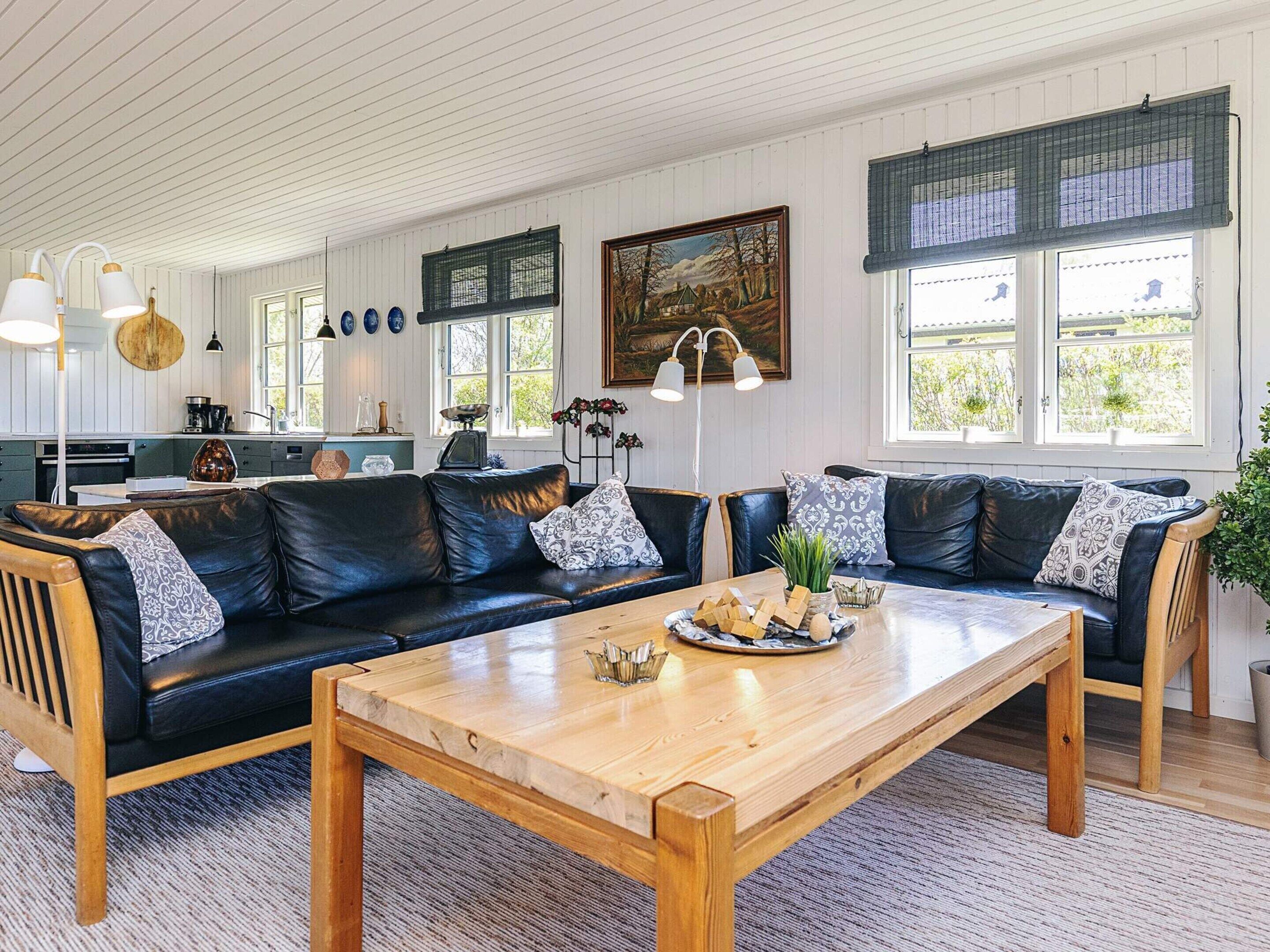 A modern living room with a wooden coffee table, black leather sofas, and a kitchen in the background.
