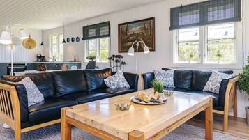 A modern living room with a wooden coffee table, black leather sofas, and a kitchen in the background.