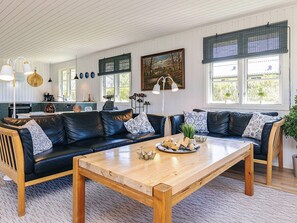 A modern living room with a wooden coffee table, black leather sofas, and a kitchen in the background. - 4 Star Holiday Home in Kirke Hyllinge (Kirke Hyllinge)