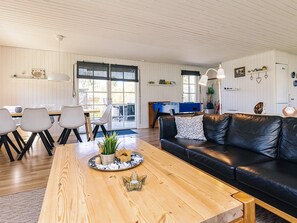 A cozy living room with a wooden coffee table, a black leather sofa, and a dining area with chairs and a table. - 4 Star Holiday Home in Kirke Hyllinge (Kirke Hyllinge)
