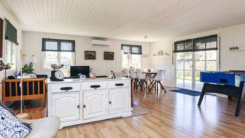 A room with a wooden floor, white walls, a dining table with chairs, a foosball table, and a crib with a changing station.