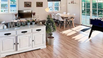 Um quarto espaçoso com piso de madeira, uma mesa de jantar com cadeiras, uma mesa de pebolim e uma grande janela com vista para áreas verdes.