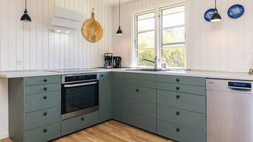 A kitchen with a built-in oven, a dishwasher, and a window with a view of greenery.