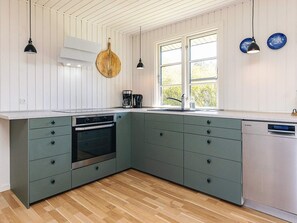 A kitchen with a built-in oven, a dishwasher, and a window with a view of greenery.
