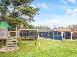 Una propiedad residencial con una casita de juegos de madera, un trampolín y una zona de estar exterior cubierta.