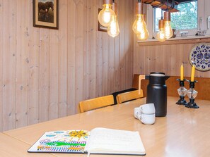 A wooden interior with a table, chairs, a book, a coffee pot, and wall-mounted light fixtures.
