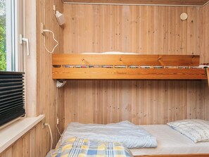 Una cama litera con cabecera de madera, una cama inferior con manta escocesa y una ventana con persianas.